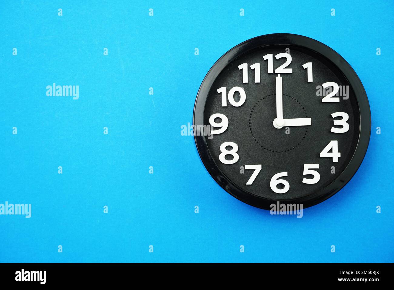 orologio rotondo nero che mostra le ore cinque su sfondo blu Foto Stock