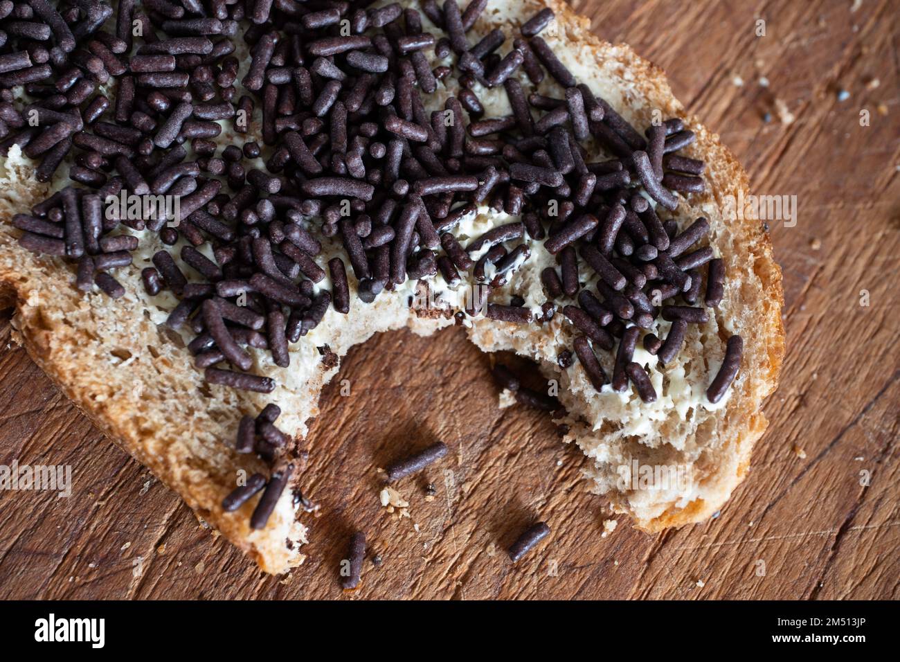 Pane integrale spalmato con burro e deliziosi spruzzi di cioccolato sulla parte superiore, su asse di legno. È stato preso un morso Foto Stock