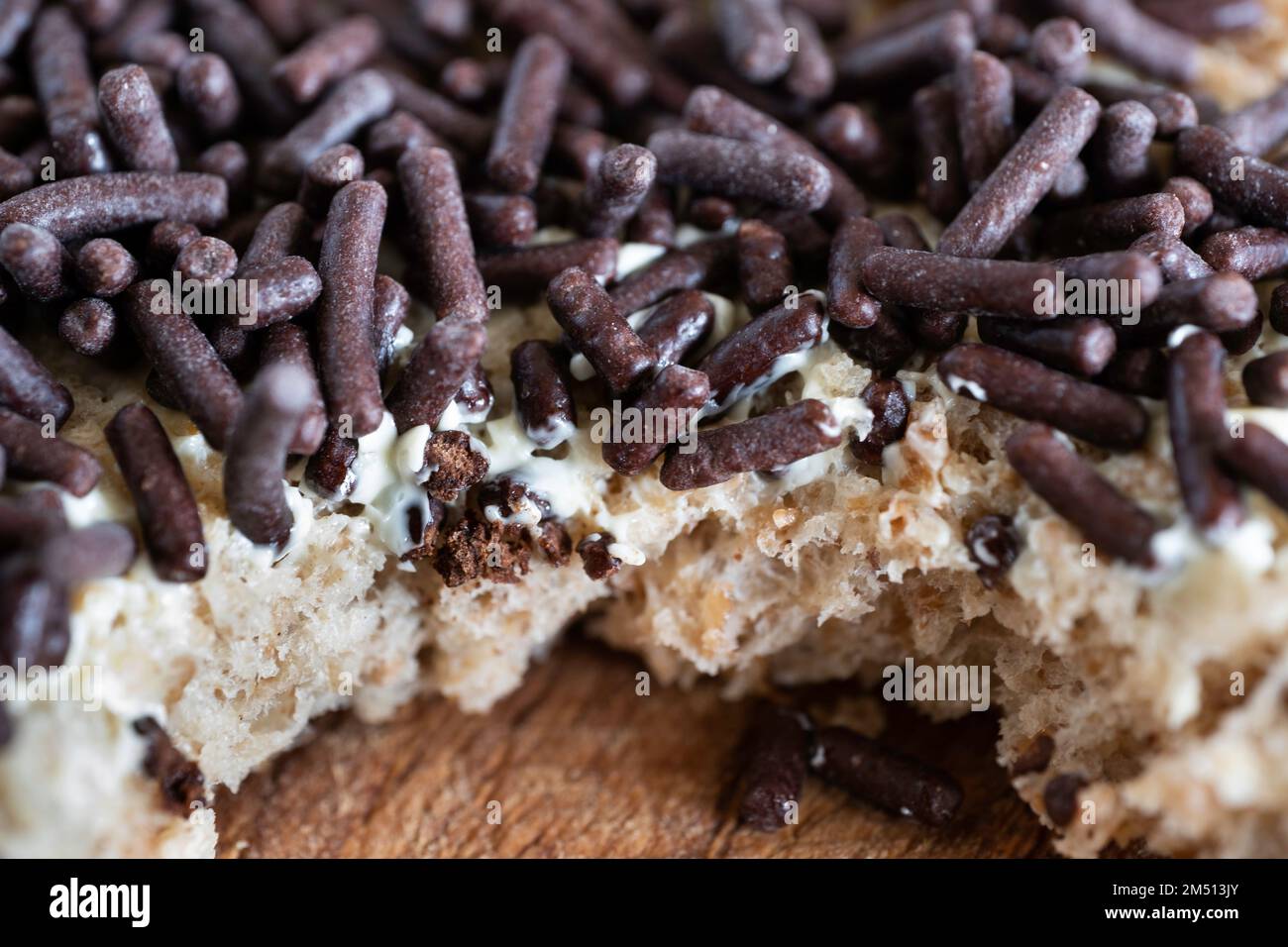 Pane integrale spalmato con burro e deliziosi spruzzi di cioccolato sulla parte superiore, su asse di legno. È stato preso un morso Foto Stock