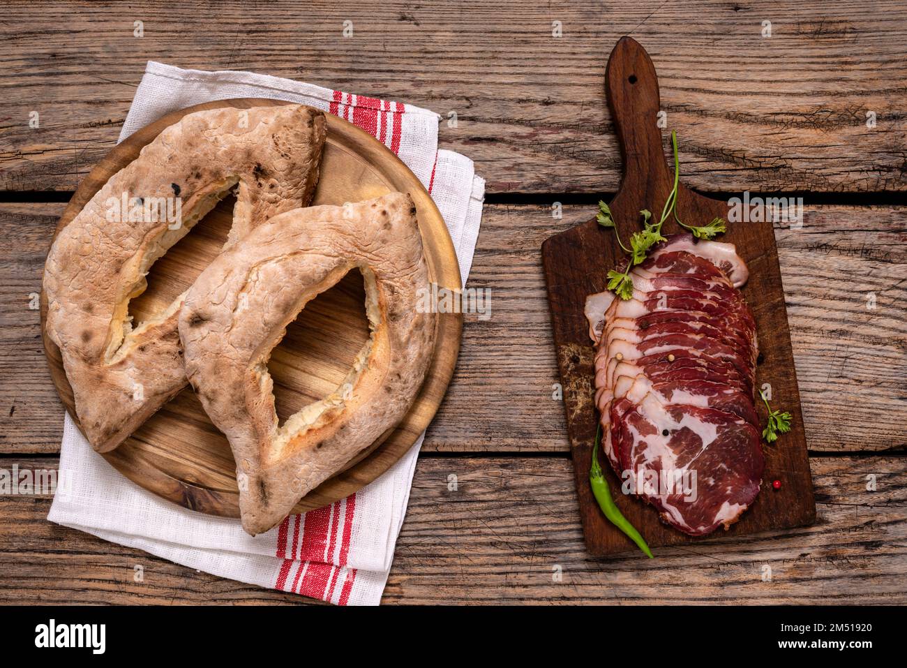 I tradizionali panini cotti in casa serbi (lepinja) e il tagliere con prosciutto affettato su un tavolo di legno. Foto Stock
