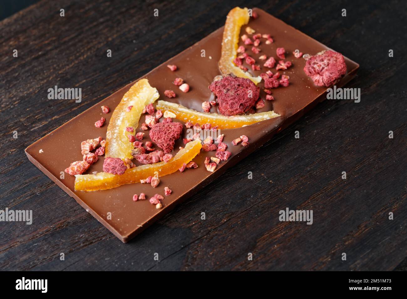 Barra di cioccolato con buccia d'arancia candita e lampone su tagliere di legno scuro Foto Stock