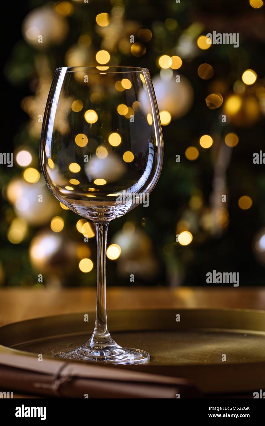 Vuoto elegante bicchiere di vino di fronte all'albero di Natale con luci di festa di Capodanno sullo sfondo Foto Stock