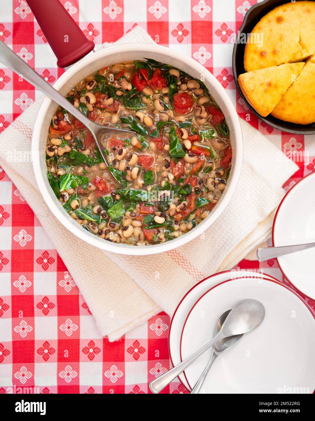 Vista dall'alto della tradizione americana del capodanno meridionale di piselli oculari neri, verdi da collard e pane di mais su un panno da tavolo rosso e bianco a scacco Foto Stock