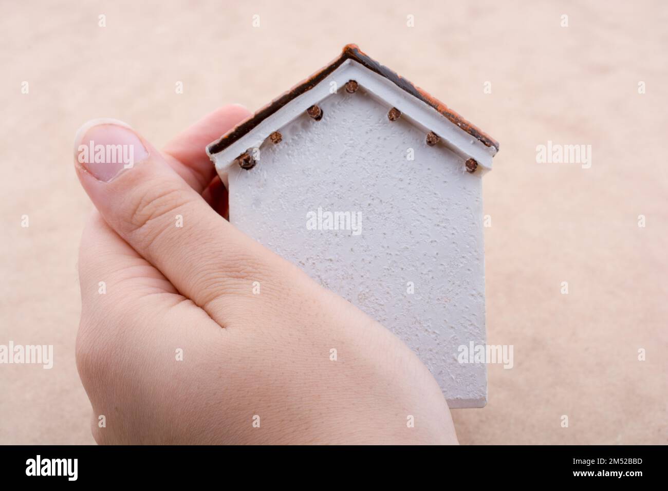 Piccola casa modello e una mano su uno sfondo di colore marrone chiaro Foto Stock