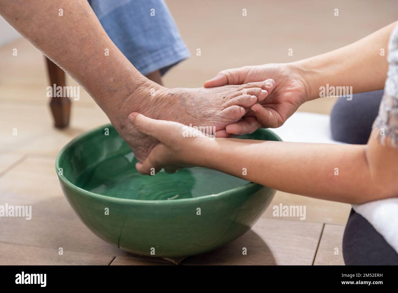 L'operatore sanitario femminile pulisce i piedi della donna anziana con un asciugamano. Foto Stock