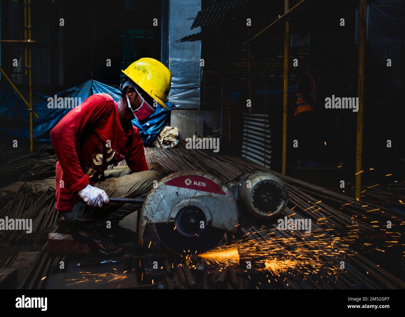 Primo piano di un addetto alle costruzioni che taglia barre di rinforzo in metallo mediante una rettificatrice Foto Stock