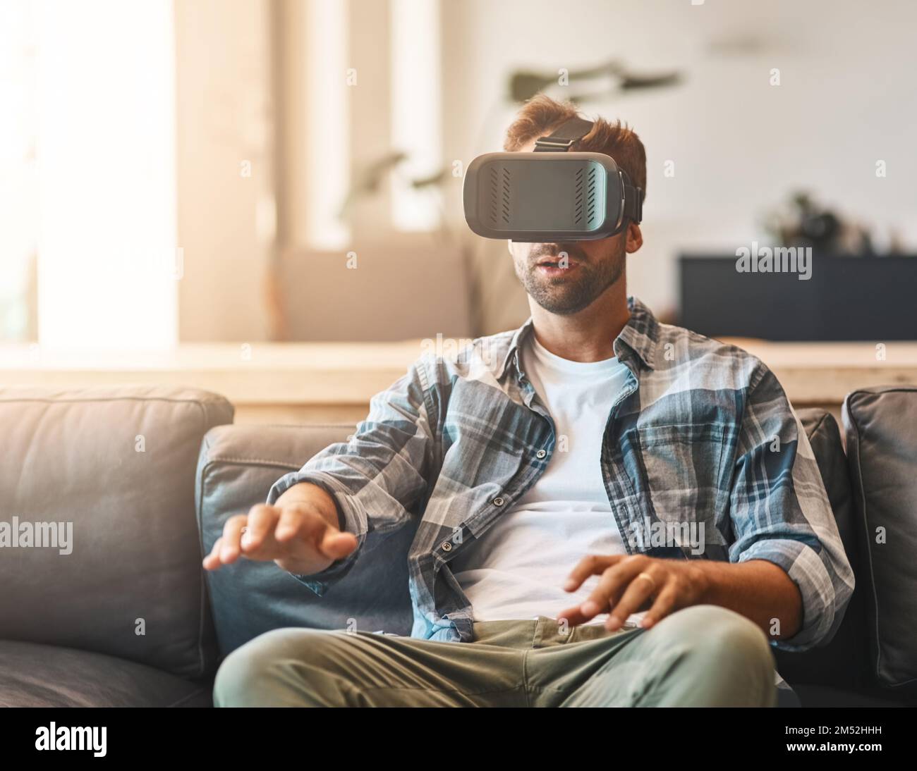 Intrattenimento per tutti i sensi. un giovane uomo che usa una cuffia per la realtà virtuale sul divano di casa. Foto Stock