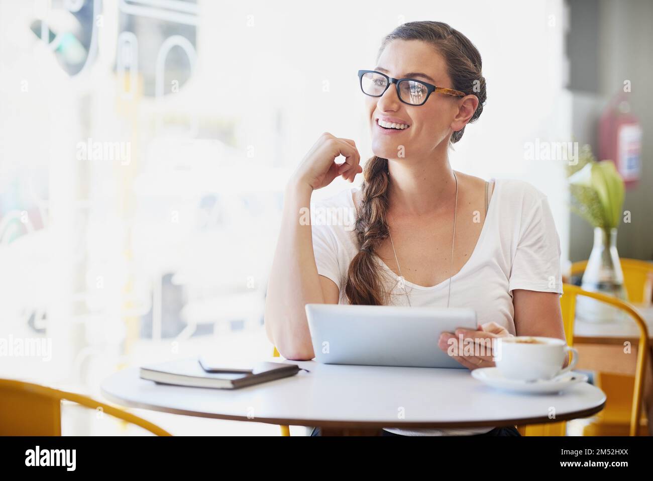 Collegato e caffeinato. una giovane donna rilassata che usa la sua tavoletta mentre beve caffè nel suo caffè preferito. Foto Stock
