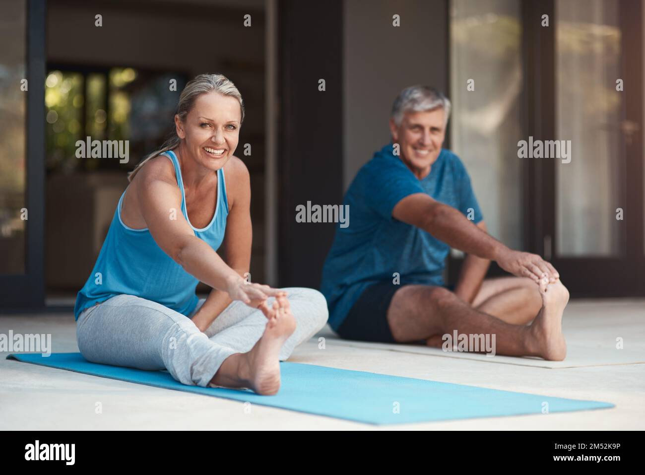 Lo stretching è importante ma anche divertente. una coppia matura e felice che si allunga prima che facciano yoga fuori della loro casa. Foto Stock