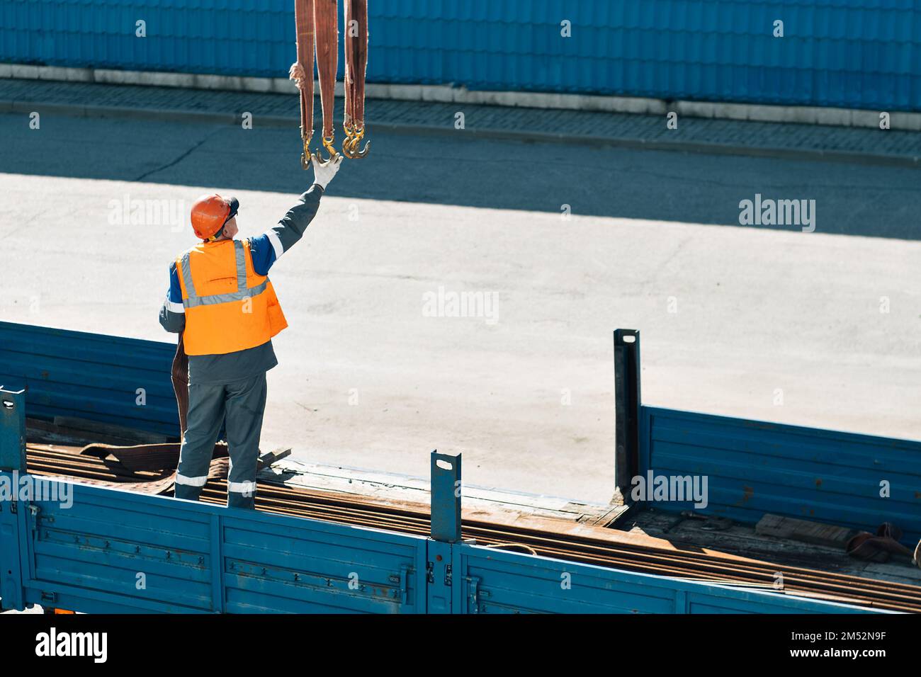 Infilare il casco e il giubbotto scarica tubi metallici e raccordi dalla carrozzeria del camion in una giornata limpida. Background di produzione. Flusso di lavoro autentico in cantiere. Slinger al lavoro.. Foto Stock