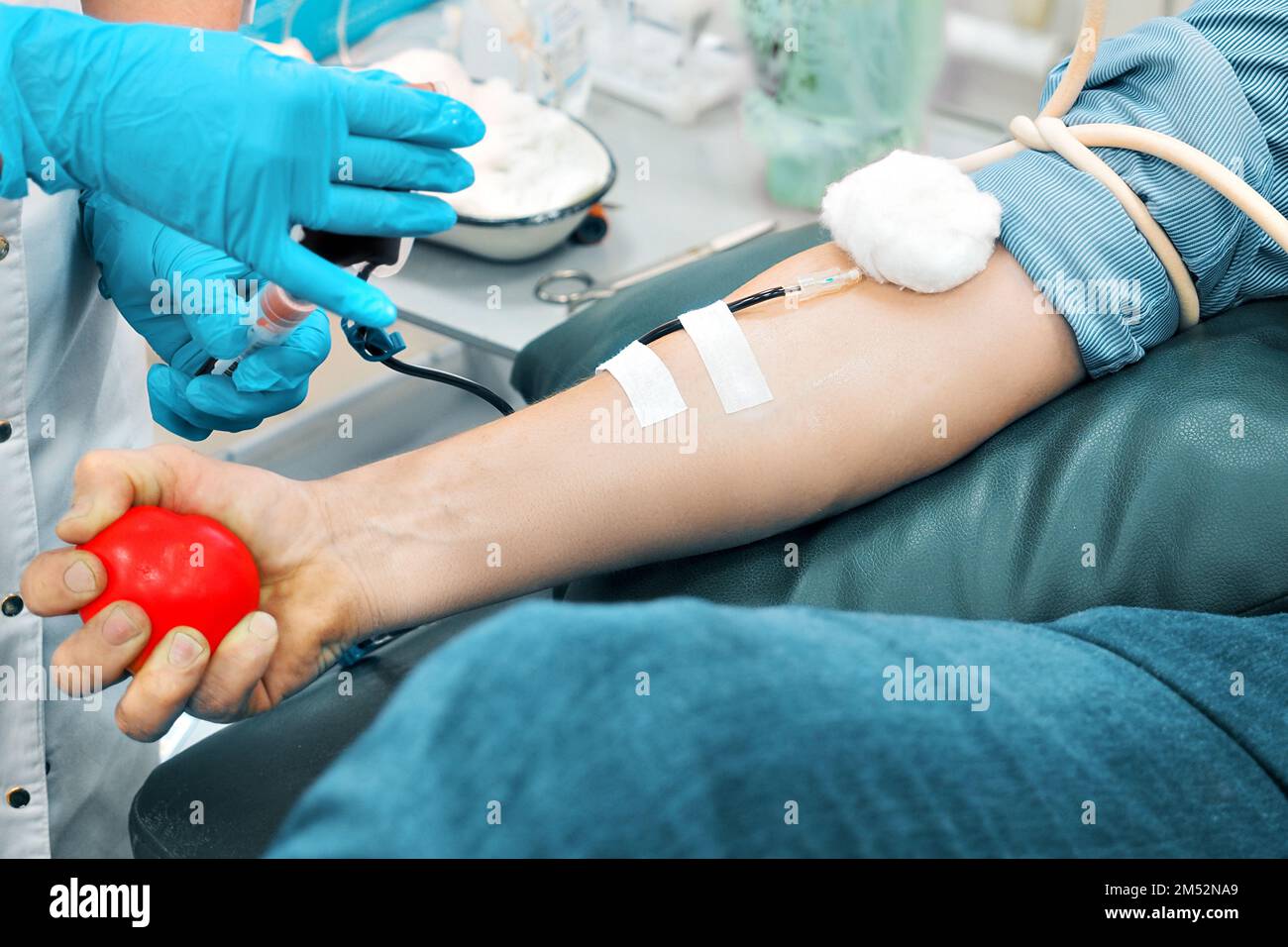 Tema della donazione. L'uomo dona sangue in ospedale. La mano dell'uomo stringe il cuore di gomma. Primo piano. Il donatore si siede sulla sedia. Sfondo.. Foto Stock