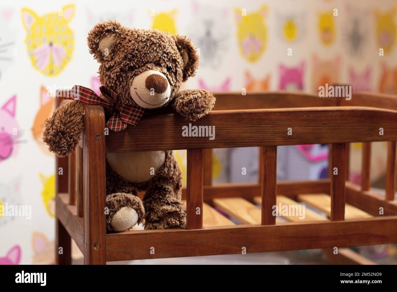 un morbido orsetto di orsacchiotto marrone si siede in un letto di legno per bambini in una stanza per bambini su uno sfondo sfocato Foto Stock