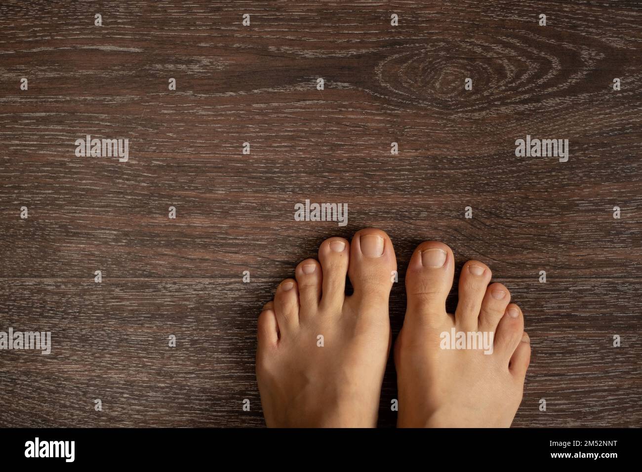 gambe femminili senza scarpe su un pavimento di legno marrone, vista dall'alto verso il basso Foto Stock