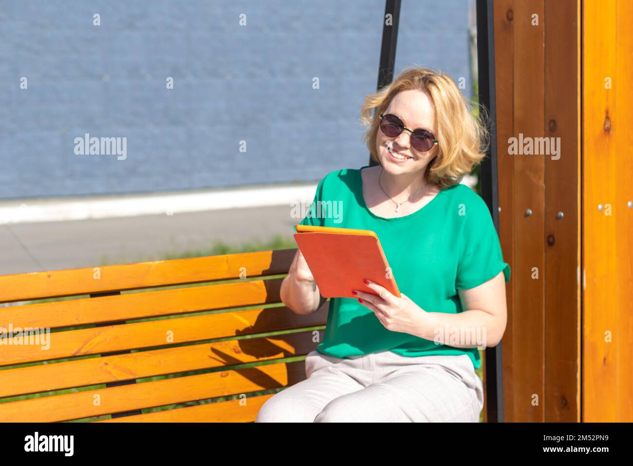 Ritratto di una studentessa sorridente che indossa occhiali da sole, tenendo in mano un moderno tablet digitale per strada. Una ragazza attraente che guarda il camer Foto Stock