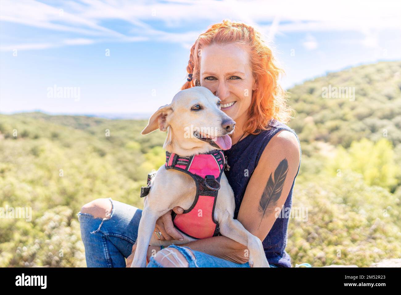 Donna che abbraccia un cane mentre si siede in montagna Foto Stock
