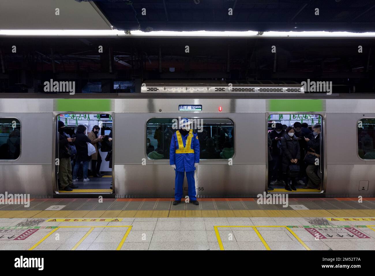 Un vecchio uomo giapponese che lavora come guardia di sicurezza sulla piattaforma della Stazione di Shibuya di fronte ad un treno della linea JR Yamanote, Tokyo, Giappone. Foto Stock