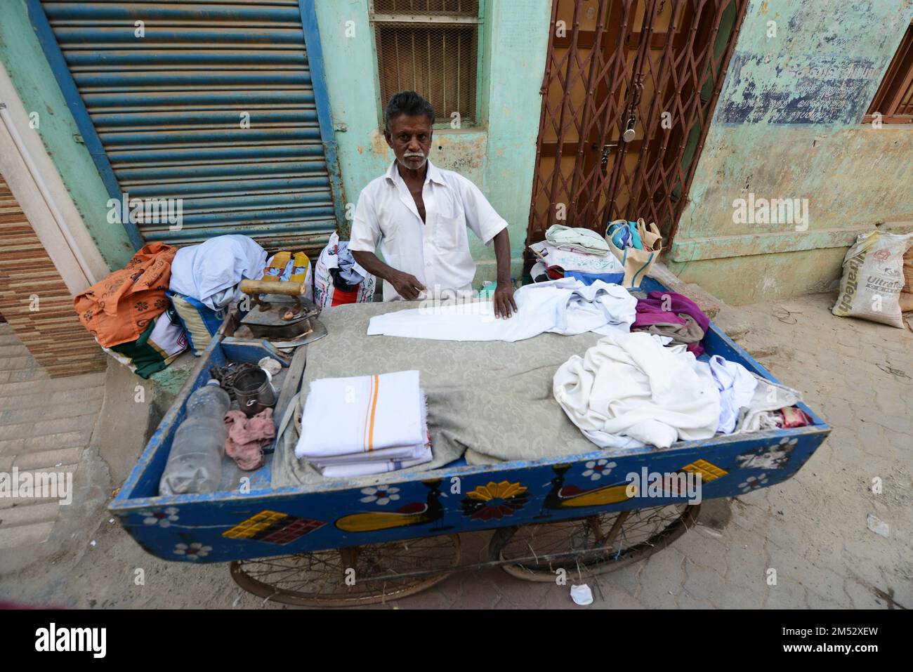 Un uomo Tamil che stira vestiti sul suo carrello mobile a Madurai, Tamil Nadu, India. Foto Stock