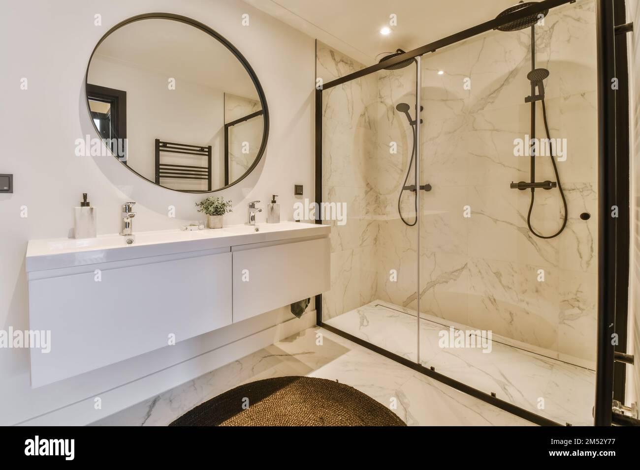 un bagno moderno con pavimento in marmo e specchi incorniciati neri sulla parete sopra la vasca e' uno specchio ovale Foto Stock