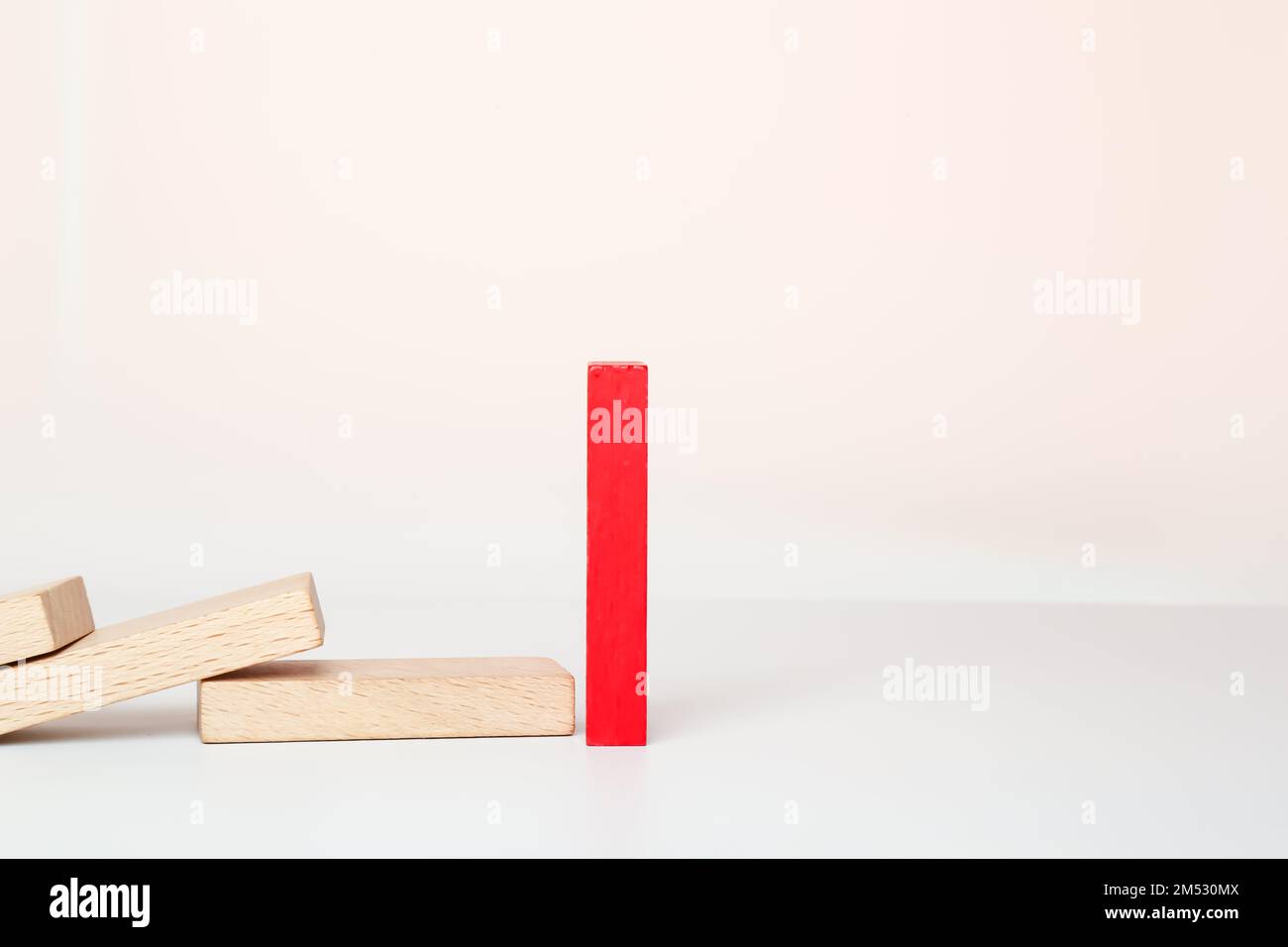 Un domino rosso si alza, e altre domino di legno cadono in fila. Reazione a catena, effetto domino su sfondo bianco. Foto Stock