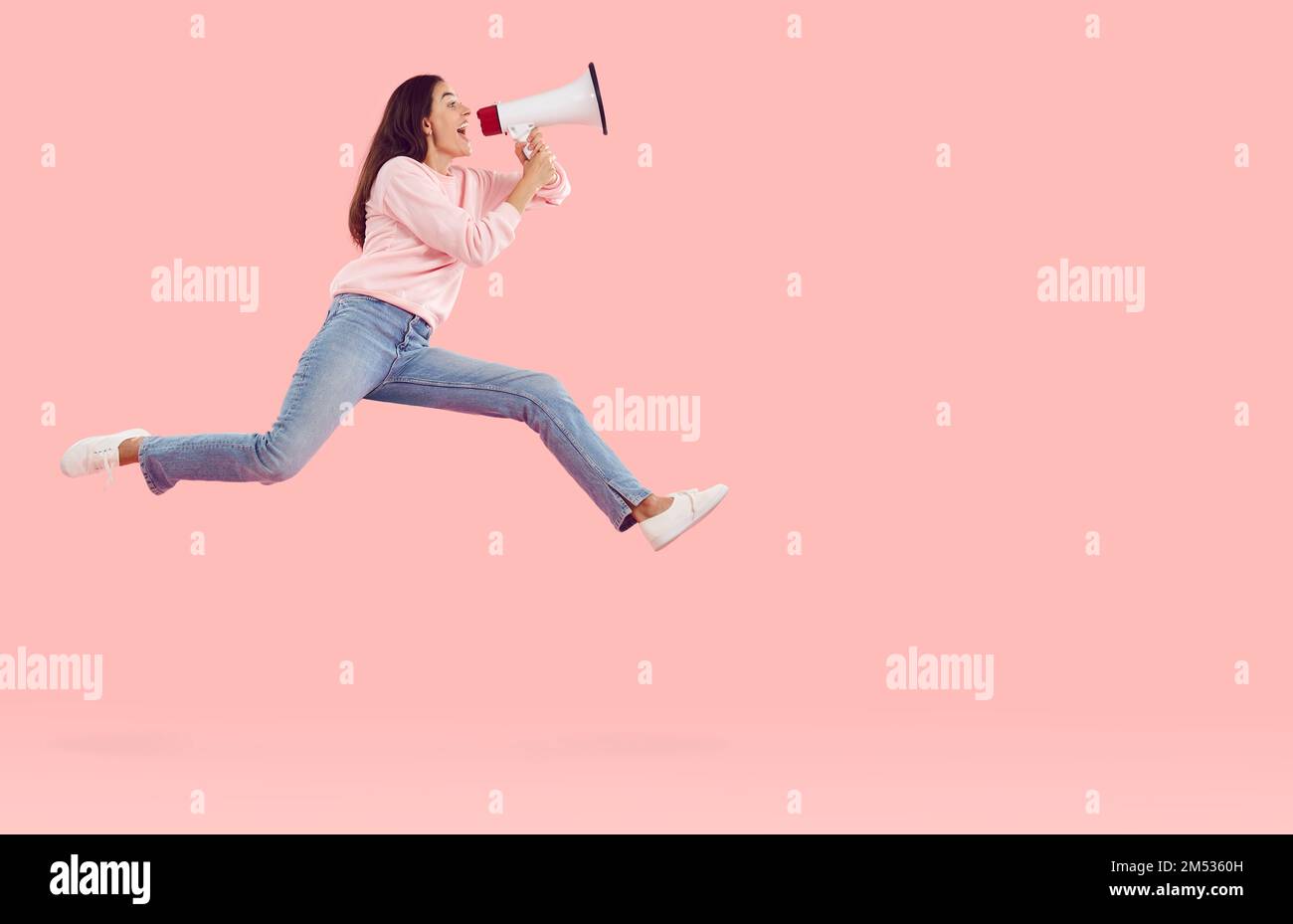 Felice donna eccitata urlare attraverso megafone mentre saltando su sfondo di colore rosa Foto Stock
