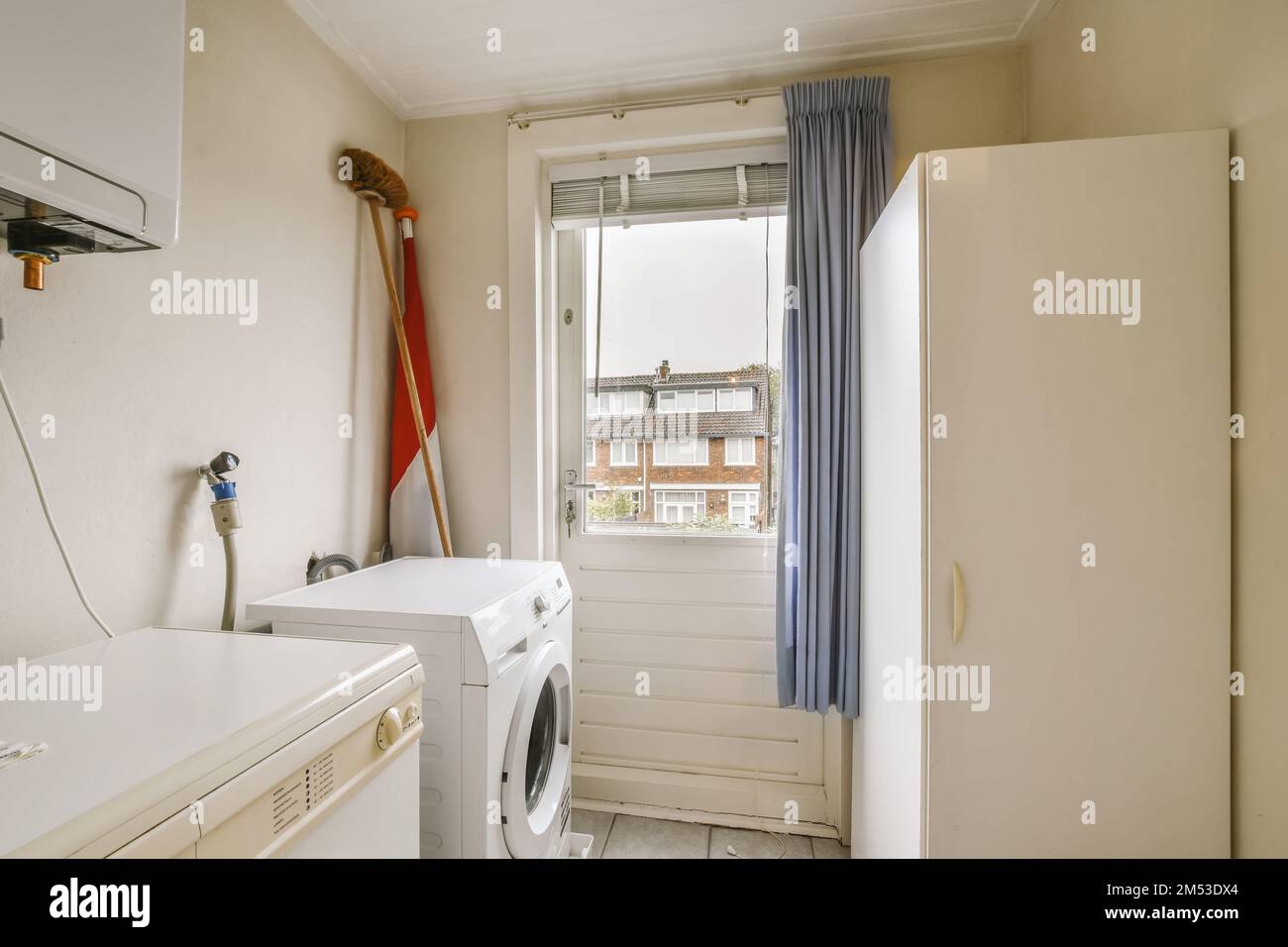 una piccola lavanderia con una lavatrice e asciugatrice nell'angolo, accanto ad una finestra che si affaccia sulla strada Foto Stock