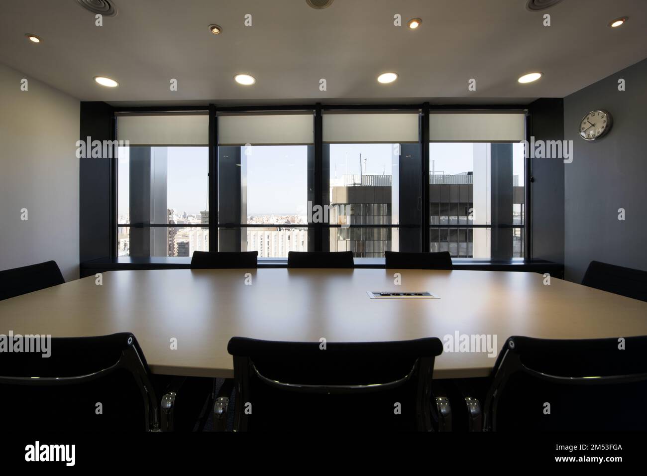 Sala riunioni con lungo tavolo in legno con sedie girevoli nere e parete di finestre con vista sulla città Foto Stock