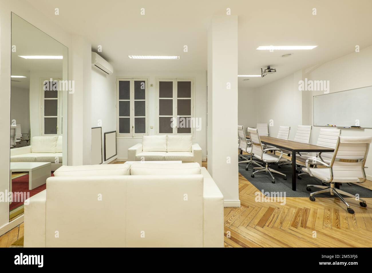 Ufficio con divani in pelle bianca, pavimenti in legno duro e un tavolo da riunione con sedie bianche girevoli Foto Stock
