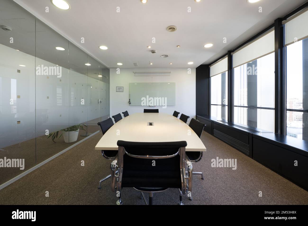 Sala riunioni con lungo tavolo in legno con sedie girevoli nere e parete con finestre Foto Stock