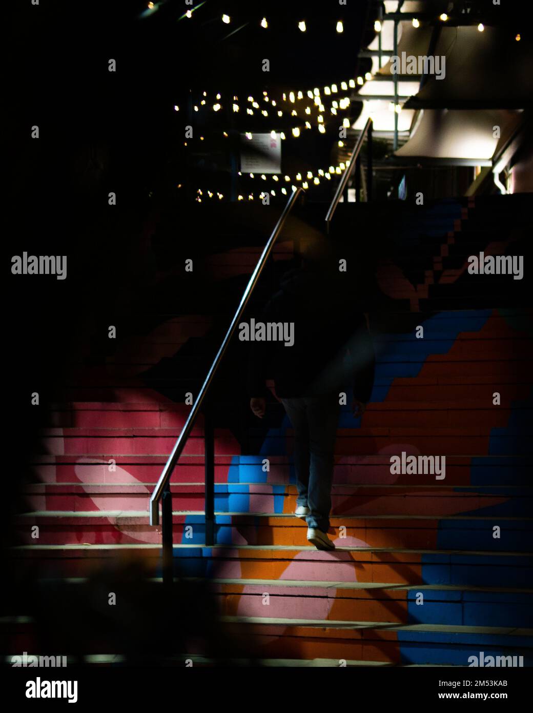 Un colpo verticale di un uomo da dietro che sale le scale colorate di notte Foto Stock