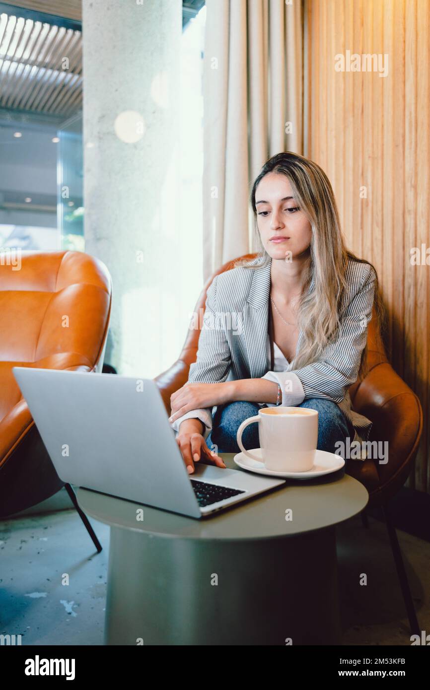 Una donna pacifica e millenaria che utilizza il computer, con una tazza di caffè in un ambiente di lavoro moderno. Foto Stock