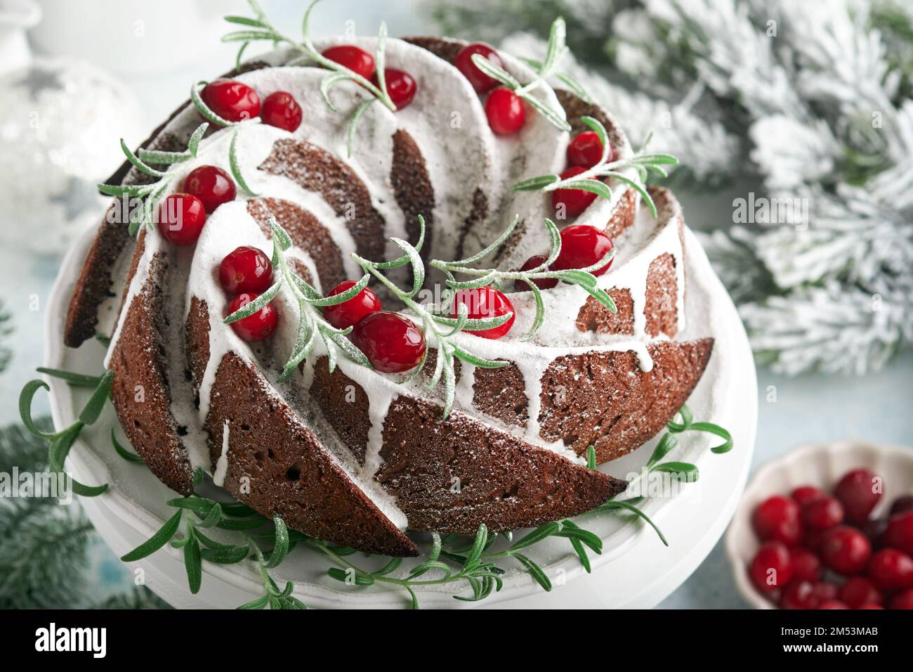 Torta al cioccolato di Natale. Tradizionale torta di frutta di Natale con smalto bianco, mirtilli rossi e rosmarino su stand bianco con decorazione natalizia. Foto Stock