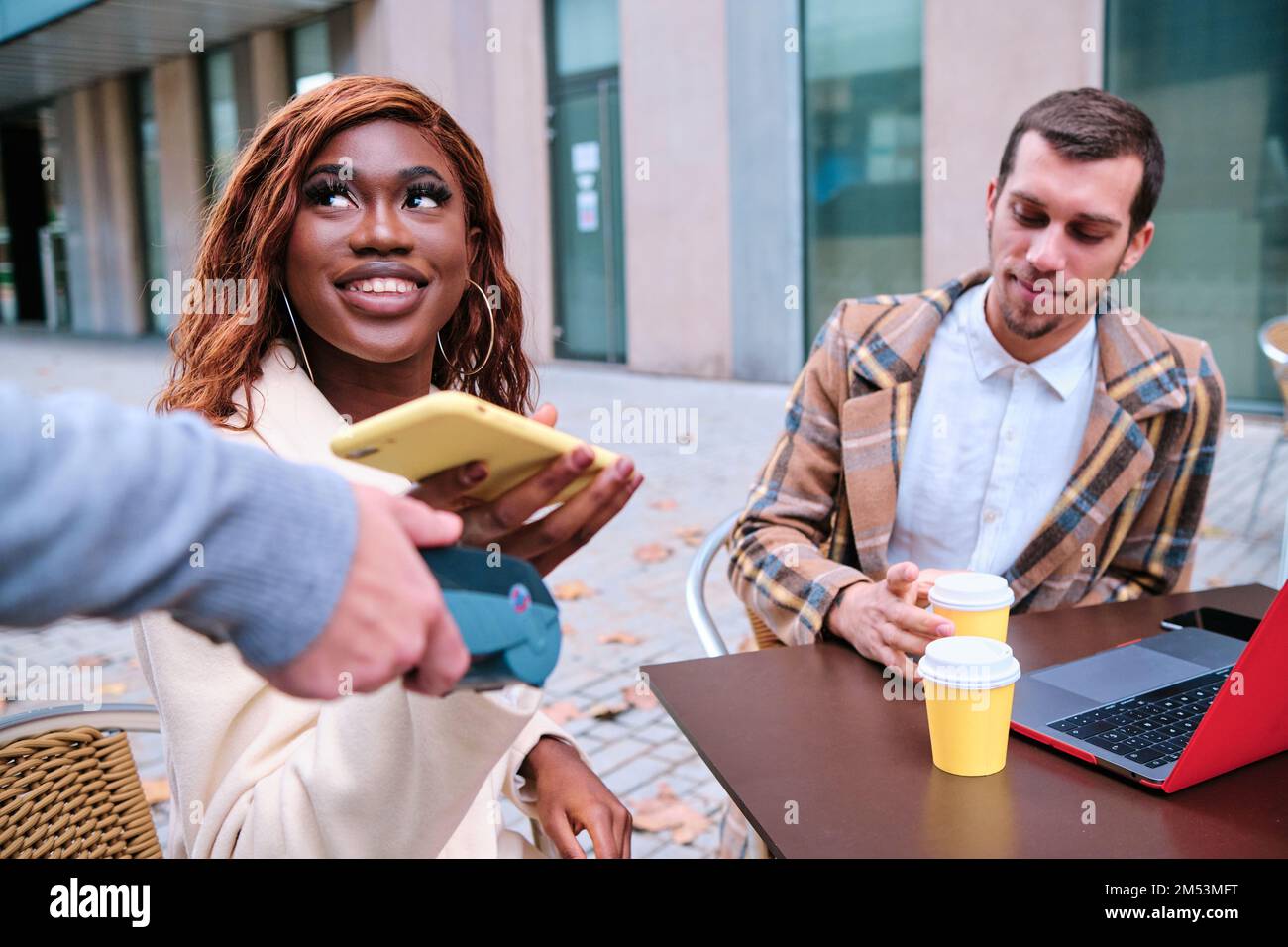 Donna sorridente mentre effettua il pagamento contactless con un telefono cellulare in una caffetteria. Foto Stock