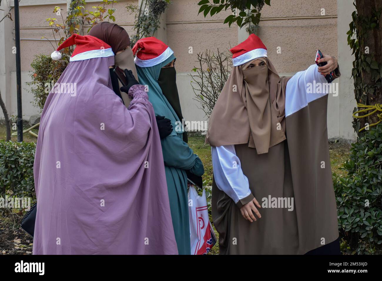 Srinagar, India. 25th Dec, 2022. Kashmiri donne musulmane velate che indossano le berrette di Santa Clause prendono un selfie dopo le preghiere alla Chiesa Cattolica della Sacra Famiglia durante le celebrazioni natalizie a Srinagar. La regione himalayana del Kashmir ha una popolazione minuscola di cristiani, centinaia dei quali si uniscono alla messa nella chiesa cattolica della Sacra Famiglia il Natale e pregano per la pace e la prosperità della regione. Credit: SOPA Images Limited/Alamy Live News Foto Stock