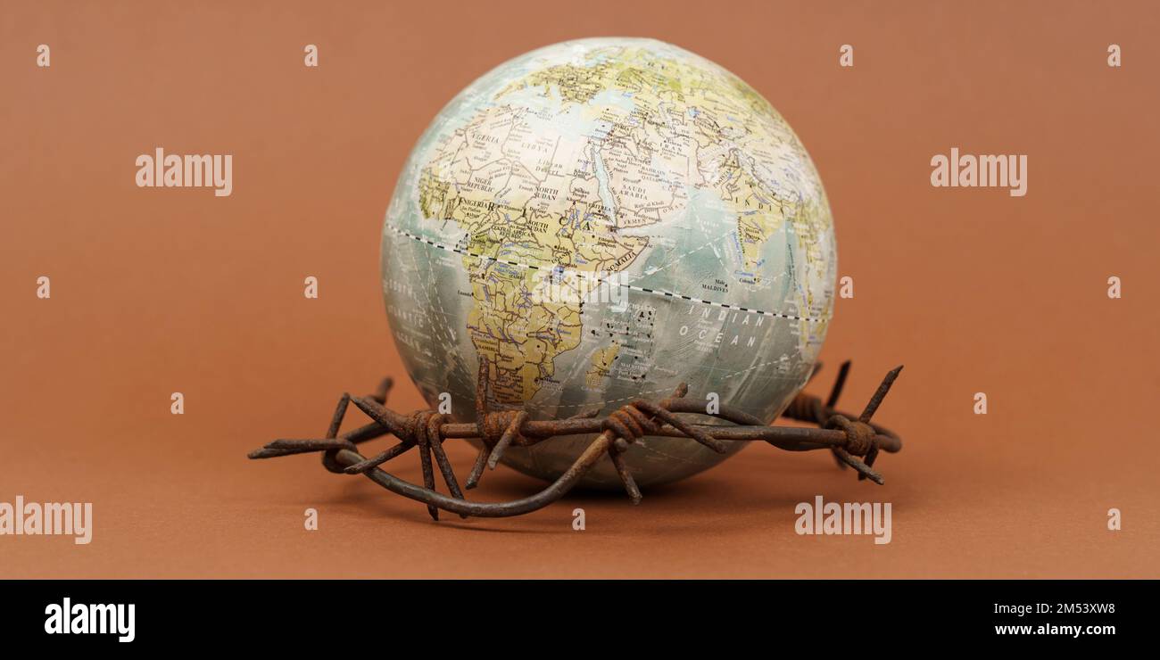Il concetto di simbolismo. Su una superficie marrone si trova un globo, che è circondato da filo spinato. Banner. Foto Stock
