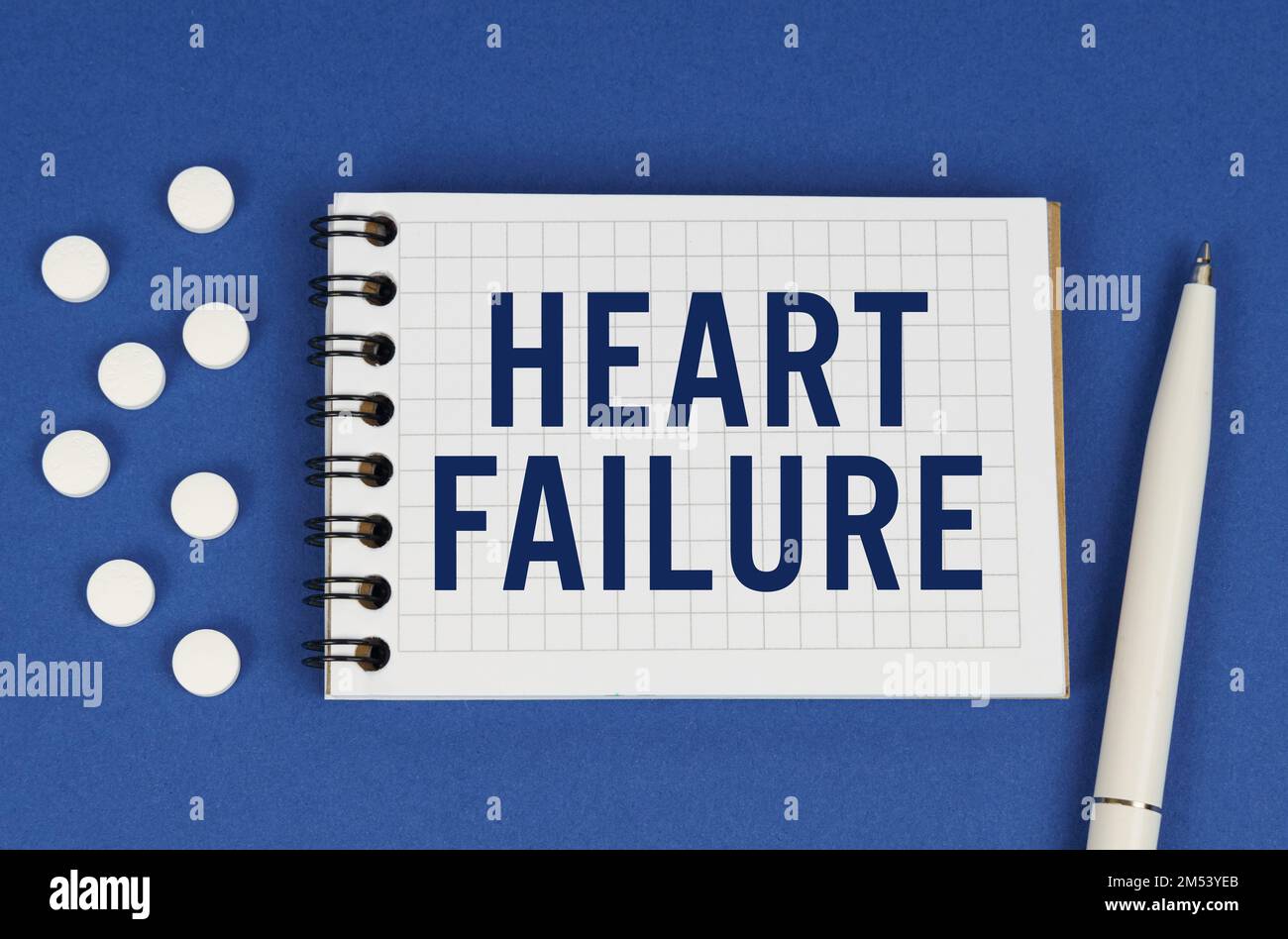 Concetto medico. Su uno sfondo blu, una penna, compresse e un blocco note con l'iscrizione - INSUFFICIENZA CARDIACA Foto Stock