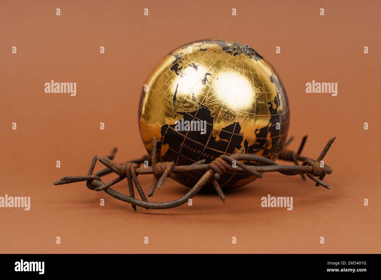 Il concetto di simbolismo. Su una superficie marrone si trova un globo, che è circondato da filo spinato. Foto Stock