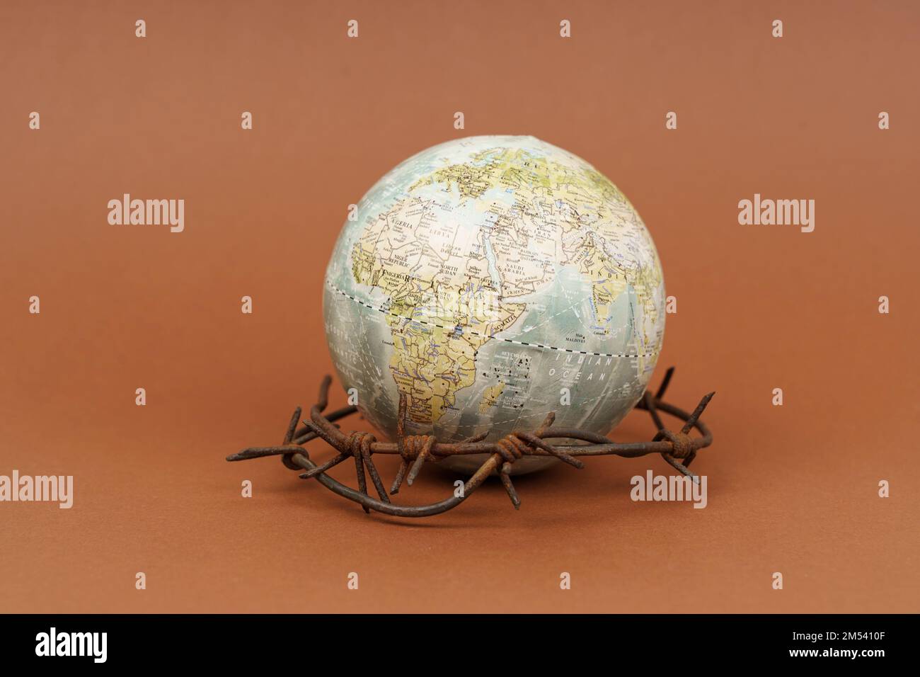 Il concetto di simbolismo. Su una superficie marrone si trova un globo, che è circondato da filo spinato. Foto Stock