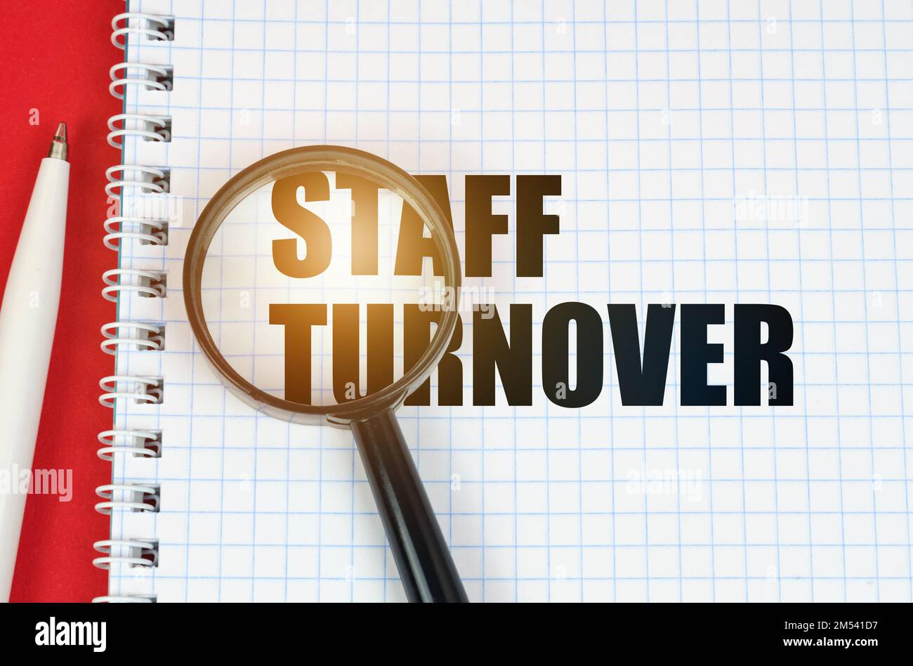 Concetto di business e finanza. Sulla superficie rossa si trova una penna, un blocco note con l'iscrizione - turnover del personale e una lente d'ingrandimento Foto Stock