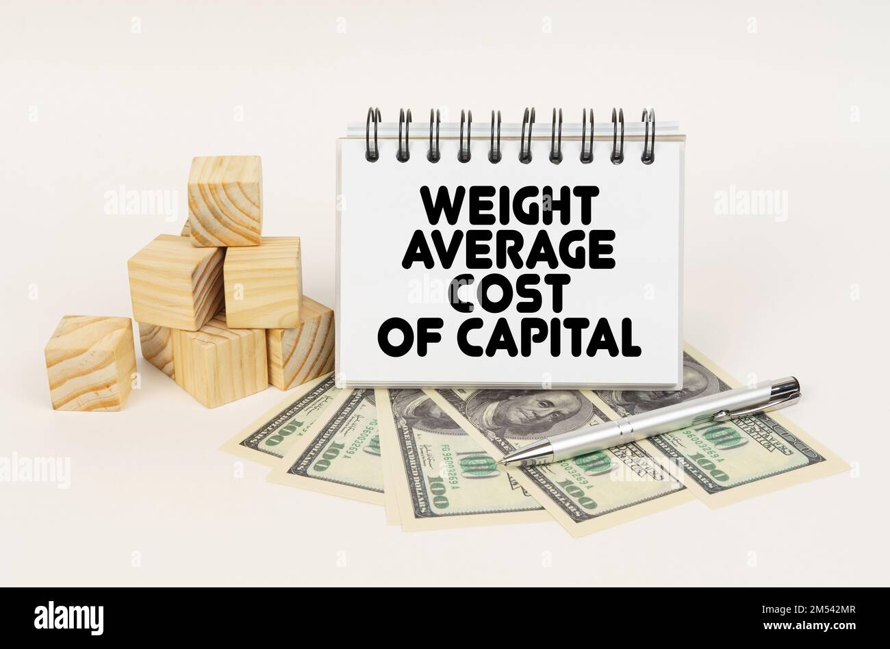 Concetto aziendale. Su una superficie bianca, cubi, dollari, una penna e un blocco note con l'iscrizione - COSTO MEDIO PONDERALE DEL CAPITALE Foto Stock