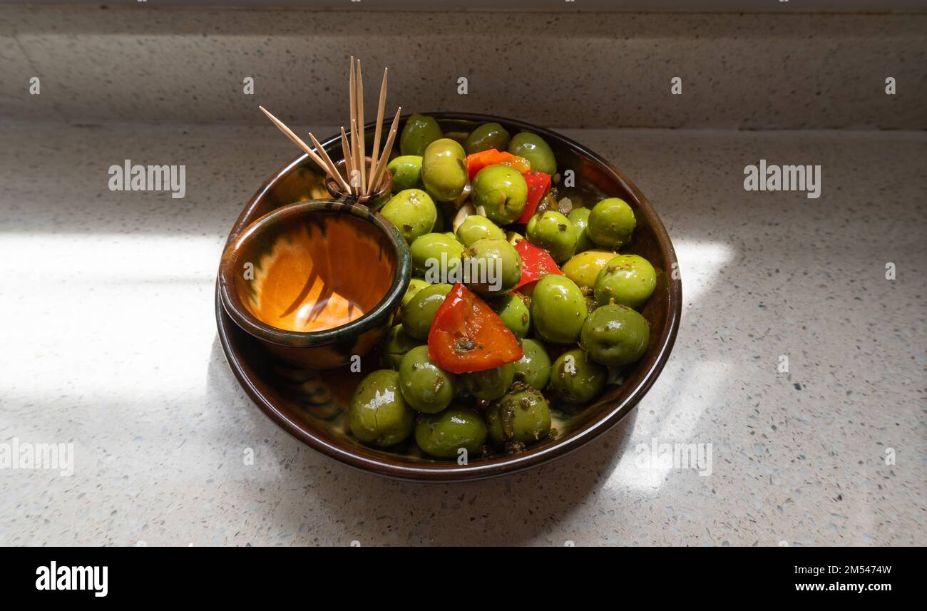 Un primo piano di una ciotola di aceitunas, olive verdi e peperoni tagliati che brilla da una superficie oleosa Foto Stock
