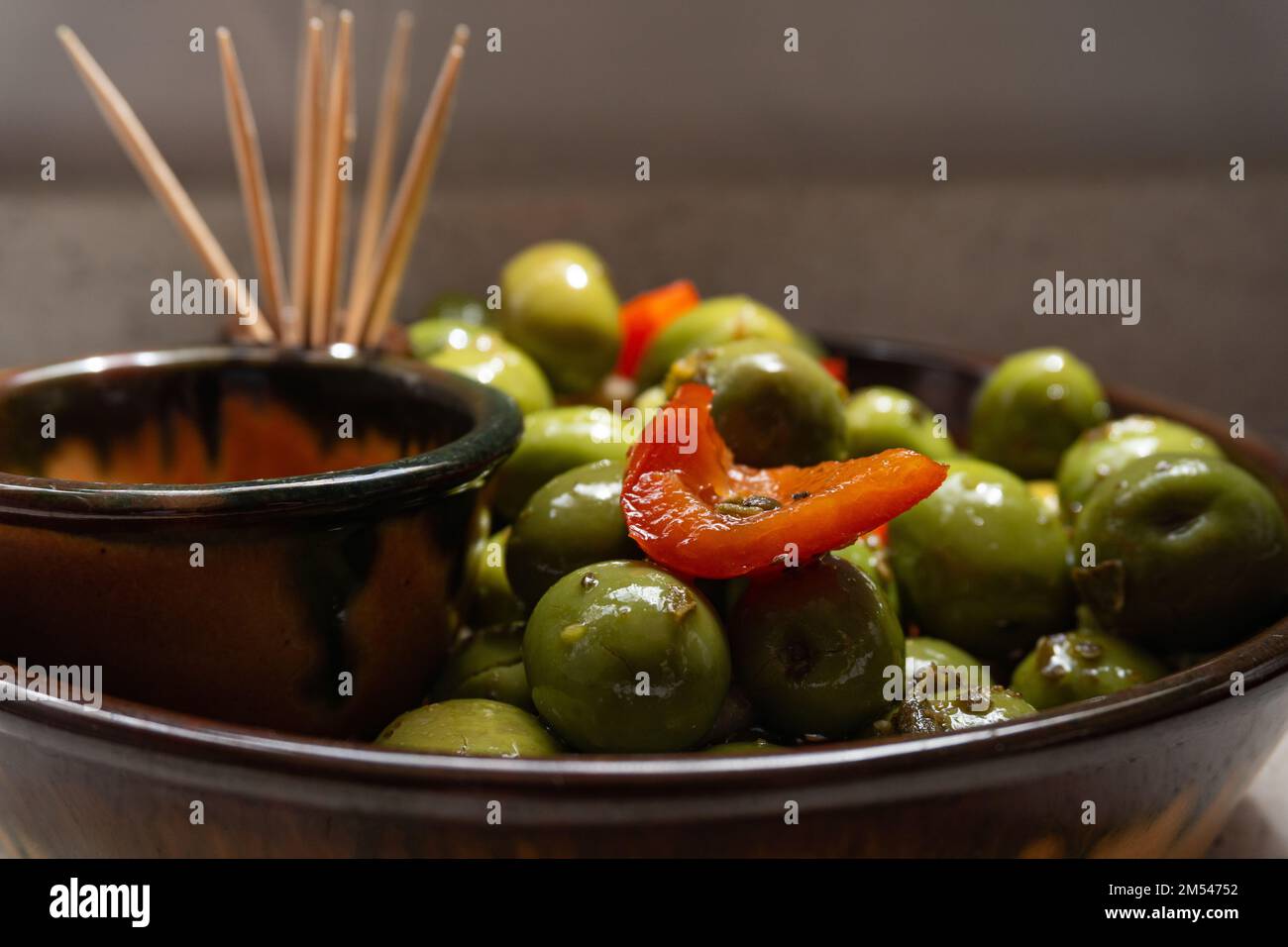 Un primo piano di una ciotola di aceitunas, olive verdi e peperoni tagliati che brilla da una superficie oleosa Foto Stock