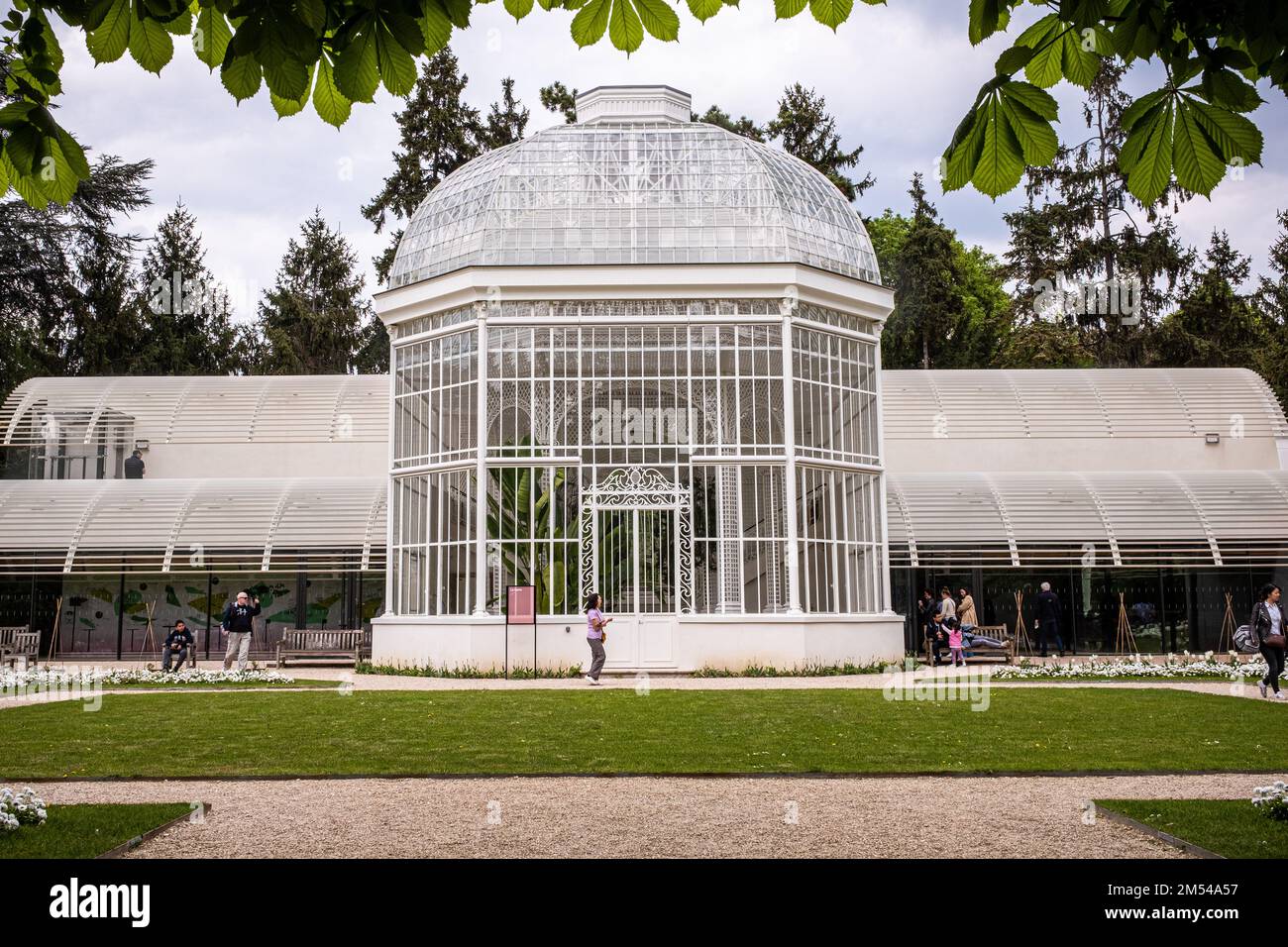 Una serra bianca in stile vittoriano con poche persone che camminano intorno. In un parco di Parigi in una giornata di primavera. Foto Stock