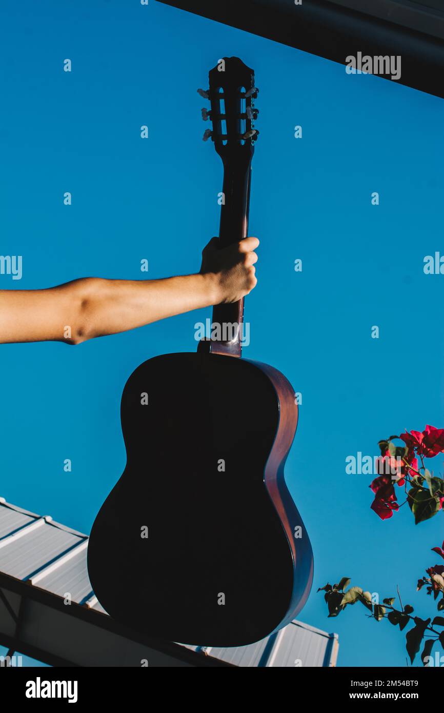 Giovane uomo salendo una chitarra acustica nel cielo blu Foto Stock