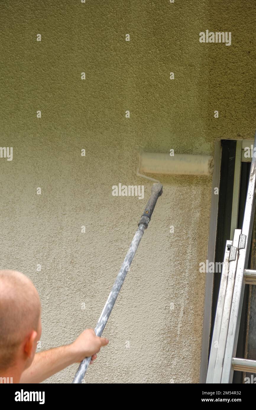 Muro painting.Building, riparare e dipingere una casa. l'uomo dipinge un muro di casa in beige con un rullo. Foto Stock