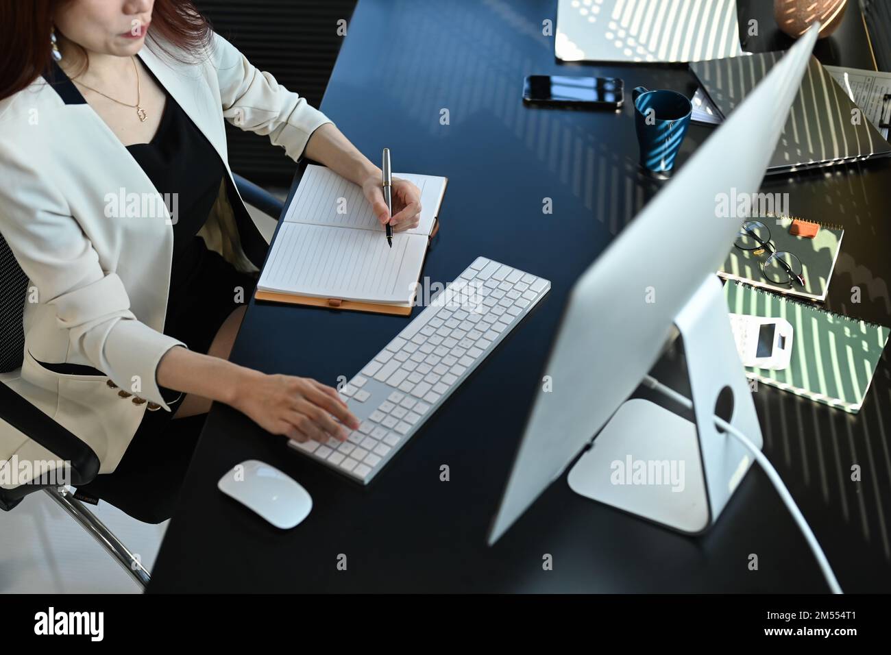 Vista dall'alto di una donna d'affari millenaria che guarda lo schermo del computer e prende appunti sul notebook Foto Stock