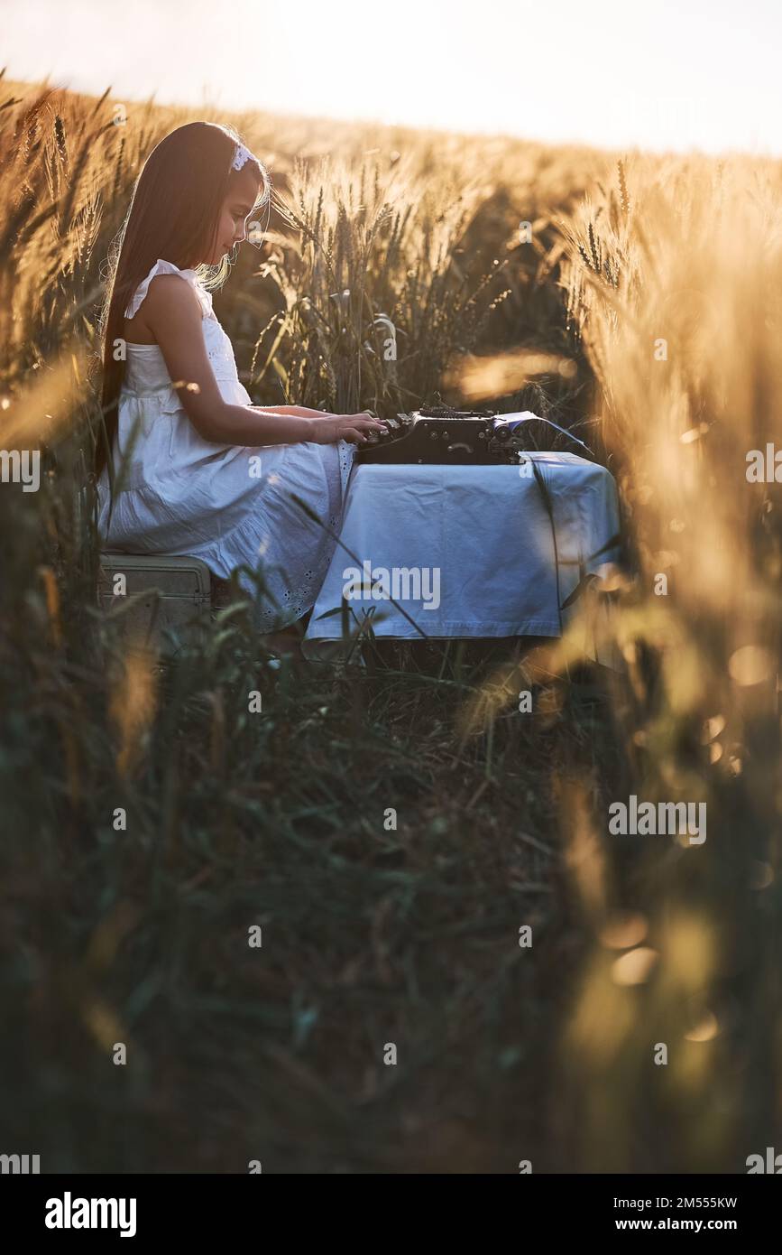 Shes pieno di idee creative. una ragazza piccola cute che gioca con una macchina da scrivere mentre si siede in un cornfield. Foto Stock