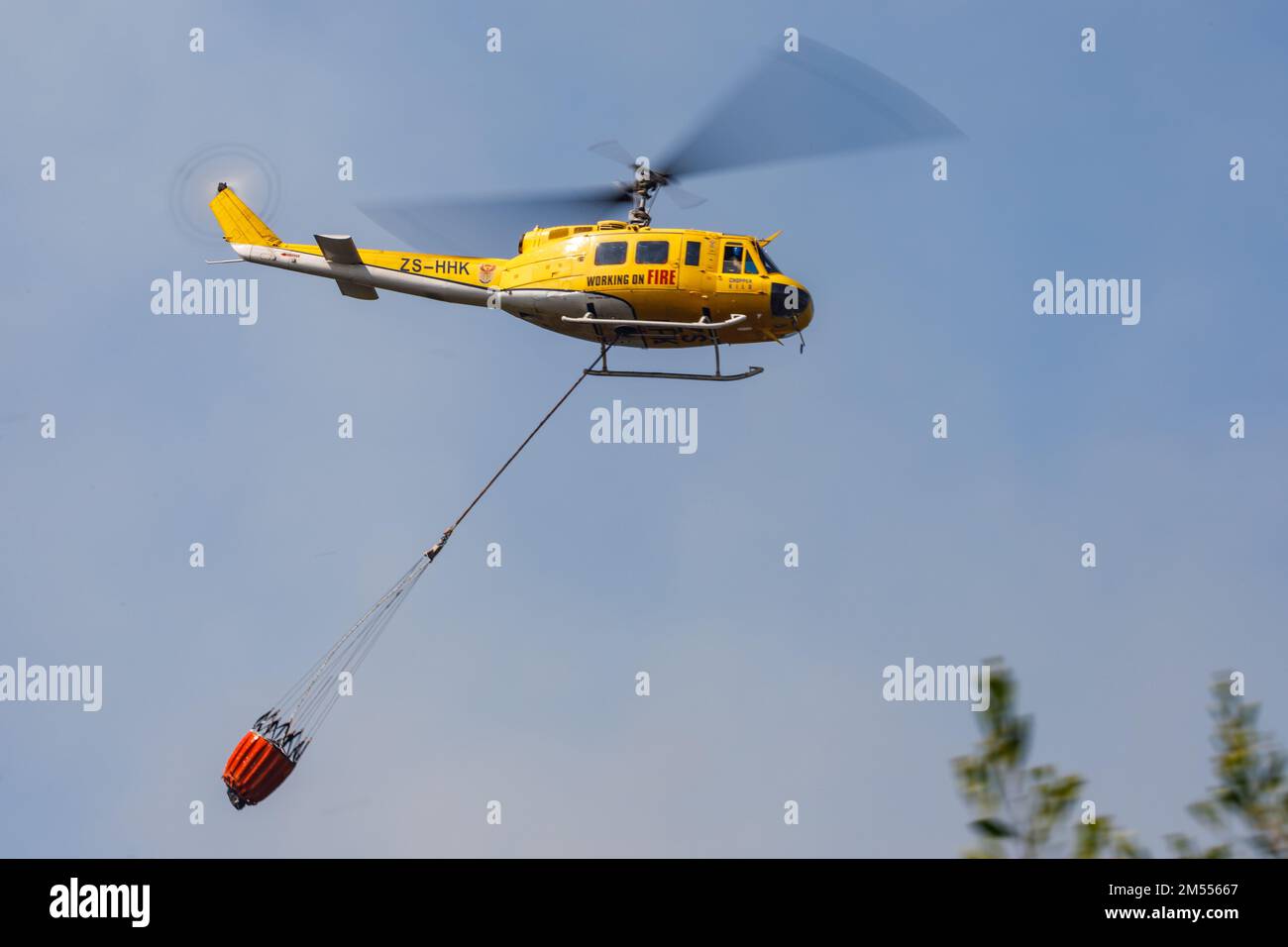 Un colpo ad angolo basso di un elicottero Huey che trasporta un contenitore d'acqua per spegnere l'incendio Foto Stock