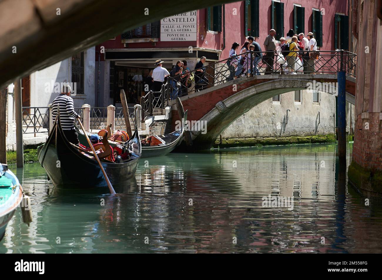 Vista sul canale di Venezia con una gondola in primo piano e diversi turisti che attraversano un ponte, Venezia, Italia Foto Stock