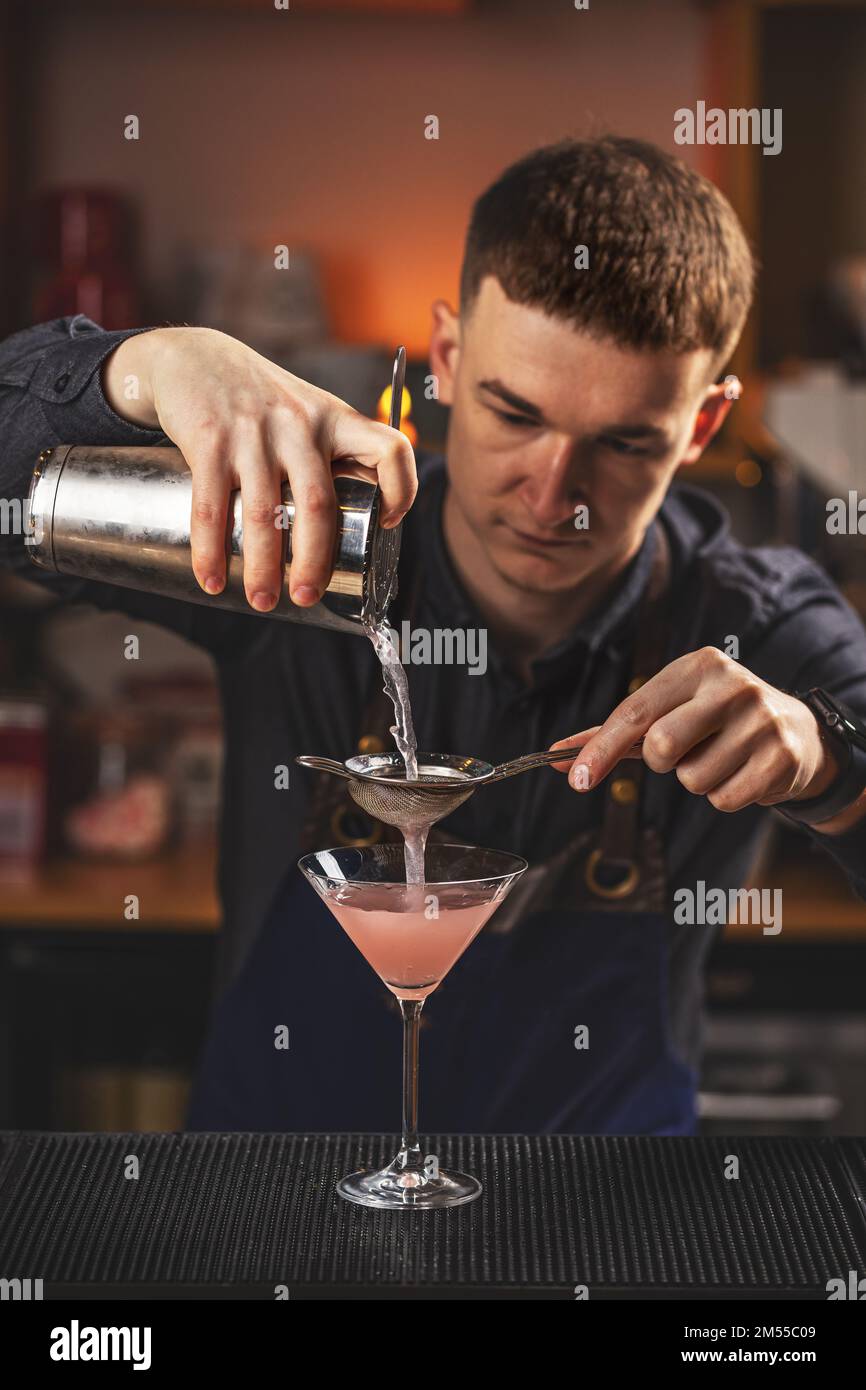 Primo piano dettagli del barman che versa vodka cosmopolita cocktail in martini vetro Foto Stock