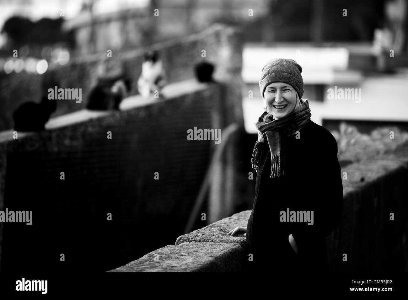 Una donna ride mentre si trova in piedi per strada. Ci sono molti gatti sullo sfondo nella sfocatura. Foto in bianco e nero. Foto Stock